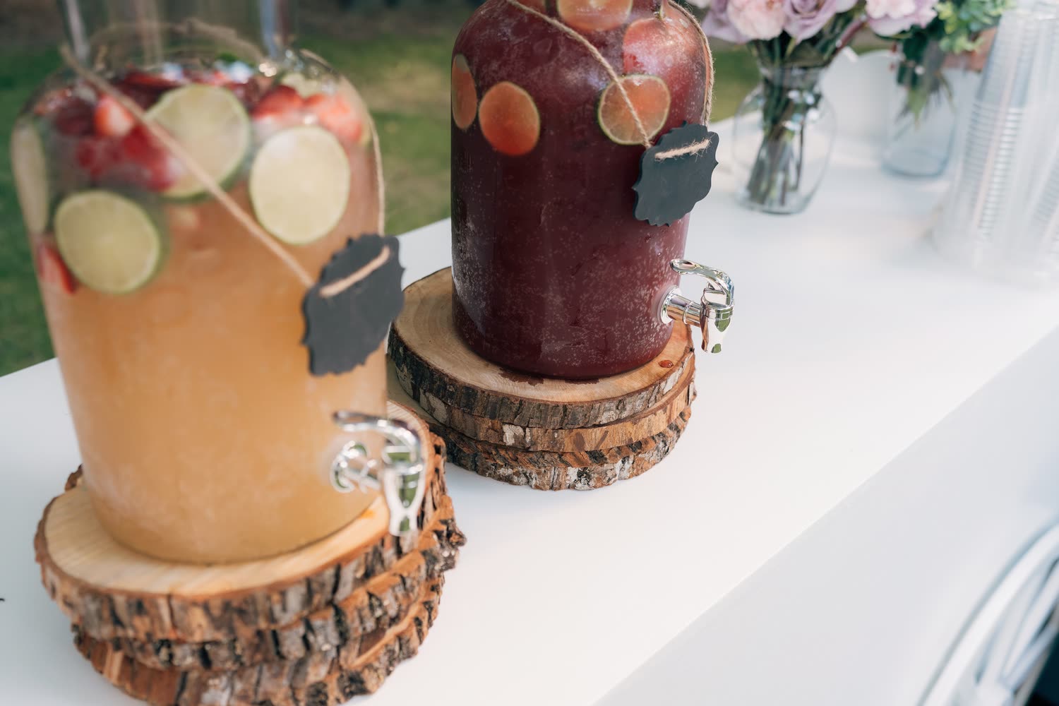 Dois garrafões de limonada com frutas e torneira, sobre troncos de madeira