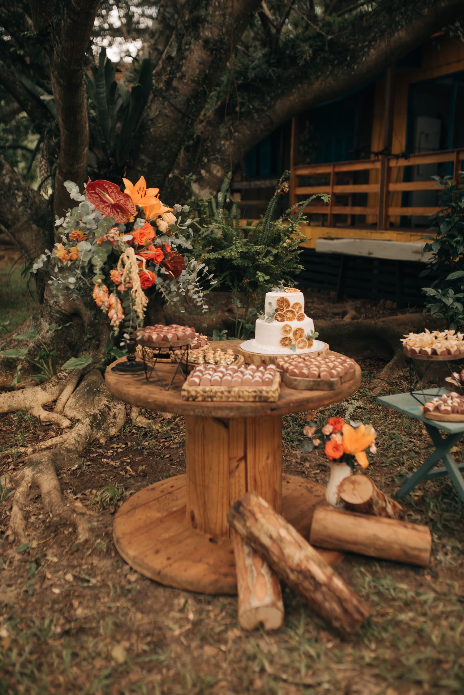 Bolo e doces sobre uma mesa rústica de madeira, com flores, ao ar livre